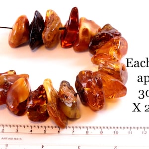 May include: A necklace of amber beads in shades of brown and orange. Each bead is approximately 30mm x 20mm. The beads are strung on a black cord. The image includes text indicating the size of each bead.