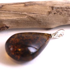 May include: A teardrop-shaped amber pendant with a silver bail. The amber is a dark brown colour with flecks of gold.