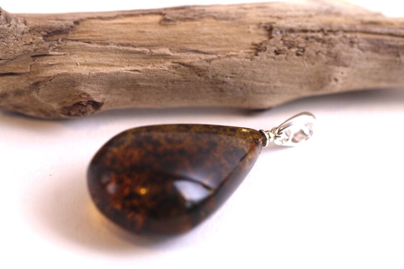 May include: A teardrop-shaped amber pendant with a silver bail. The amber is a dark brown colour with flecks of gold.
