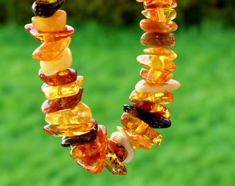 May include: A necklace composed of numerous irregular, polished amber beads in varying shades of translucent yellow, orange, and deep brown. The beads are strung together in a continuous loop, showcasing natural variations in color and shape.
