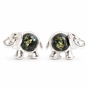 May include: A pair of silver-toned elephant-shaped stud earrings. Each elephant features a circular, polished dark green amber cabochon set into the body, showcasing natural inclusions within the stone and a smooth, reflective metallic finish.