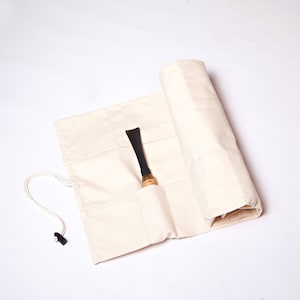 May include: A white canvas roll-up pouch with a black handle and a single wood and metal tool inside.