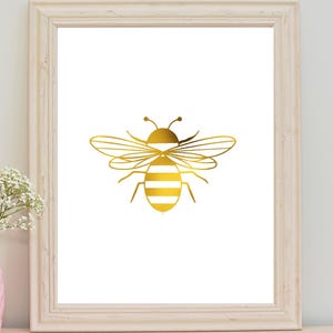 May include: A gold bee silhouette print in a white frame. The bee has white stripes on its body.