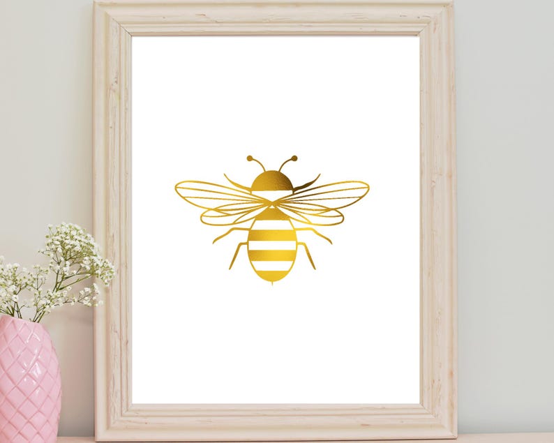May include: A gold bee silhouette print in a white frame. The bee has white stripes on its body.