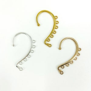 May include: Three ear cuff earring findings with five jump rings each. The findings are gold, silver, and rose gold.