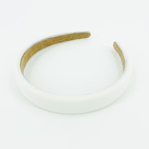 May include: A white headband with a brown suede lining. The headband is a simple, classic design.