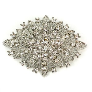 May include: A silver brooch with a large, ornate design featuring a central cluster of clear rhinestones surrounded by smaller rhinestones.