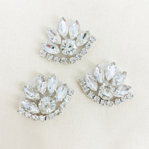 May include: Three clear crystal rhinestone embellishments in the shape of a fan. Each embellishment has a large central rhinestone surrounded by smaller rhinestones.