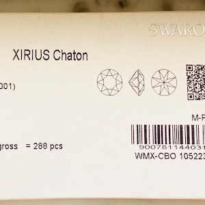 Op de afbeelding: Een close-up van een wit pakket met zwarte tekst die "1088 XIRIUS Chaton SS 29 Crystal (001) Foiled 1144031 2/00/00 gross = 288 pcs" luidt en een barcode. Het pakket bevat ook een kleine zwart-wit afbeelding van een kristal en een QR-code.