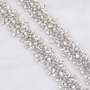 May include: Two decorative rhinestone appliques with a floral design. The appliques are made of clear, sparkling rhinestones in various shapes and sizes, arranged on a white mesh backing. Ideal for embellishing bridal wear or other garments.