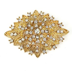 May include: A gold-toned brooch with a floral design, featuring a large central rhinestone surrounded by smaller rhinestones.