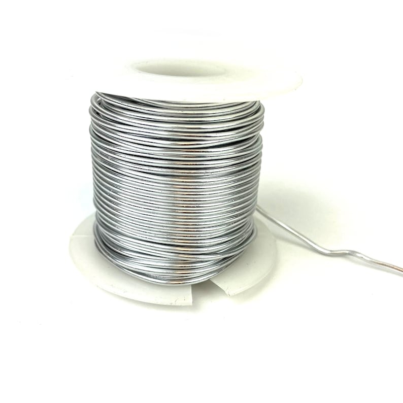 May include: A spool of silver-colored wire on a white plastic spool. The wire is wound tightly around the spool and is ready to be used for crafting or other projects.