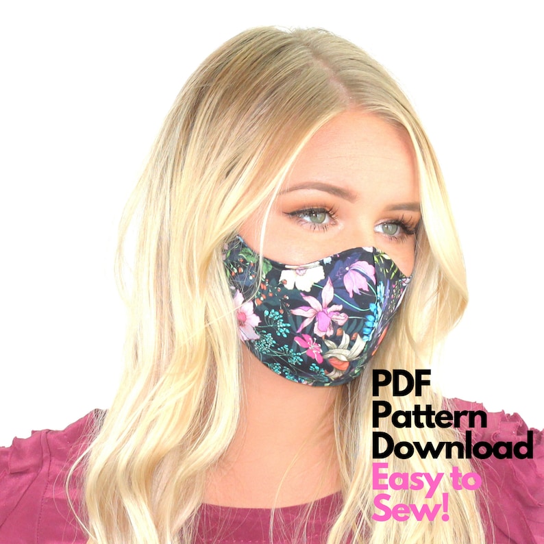 May include: A woman wearing a black face mask with a floral print. The mask has a dark background with pink, white, and blue flowers. The text "PDF Pattern Download Easy to Sew!" is in pink letters on a white background.