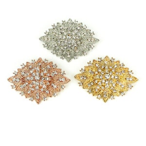 May include: Three decorative brooches with a floral design. The brooches are silver, gold, and rose gold in color and are adorned with clear rhinestones.