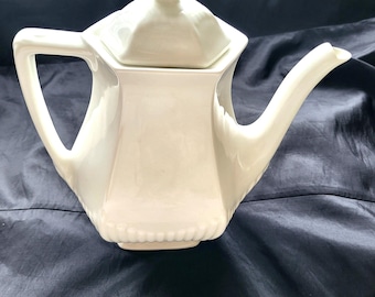 May include: White ceramic teapot with a lid and a hexagonal body. The teapot has a spout and a handle.