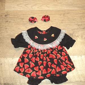 May include: A black dress featuring a watermelon slice pattern, a white lace collar, and short ruffled sleeves. The dress includes a pair of matching black bloomers with ruffled leg openings and two small circular hair accessories with red bows.