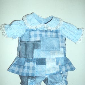 May include: A light blue doll outfit consisting of a short-sleeved top with a white lace collar and cuffs, paired with a patchwork-style tunic featuring various blue denim and plaid patterns, and matching blue patchwork bloomers with elasticized hems.