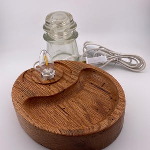 May include: A handcrafted wooden lamp base with a warm, reddish-brown finish. The base features a unique, organic shape with a small light bulb and a clear glass insulator. A white power cord with an on/off switch is attached.