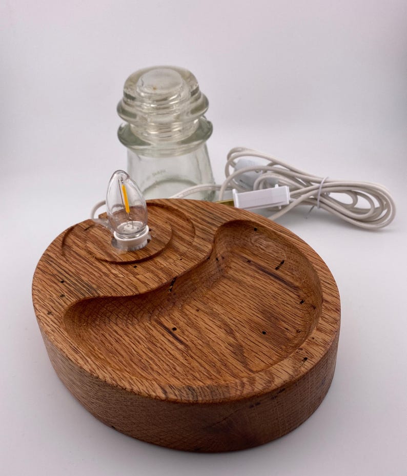 May include: A handcrafted wooden lamp base with a warm, reddish-brown finish. The base features a unique, organic shape with a small light bulb and a clear glass insulator. A white power cord with an on/off switch is attached.