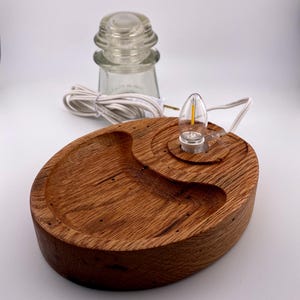 May include: A handcrafted wooden lamp base with a clear glass insulator and a small LED light. The base is oval-shaped with a carved dish and a circular area for the light. The wood has a warm, natural finish.