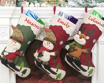 May include: Three personalized Christmas stockings with different characters. The stocking on the left has a Santa Claus character and says "Mason". The middle stocking has a snowman character and says "Emily". The stocking on the right has a reindeer character and says "Leland".