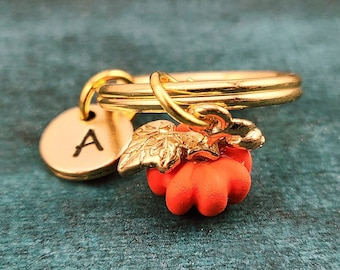 May include: Gold keyring with a small orange pumpkin charm, a gold leaf charm, and a round gold disc with the letter "A" engraved on it.