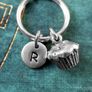 May include: Silver keychain with a cupcake charm and a round charm with the letter R. The charms are attached to a silver key ring.