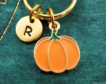 May include: Gold keychain with a pumpkin charm and a round charm with the letter R. The pumpkin is orange with a green stem.