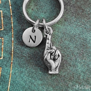 May include: Silver keychain with a charm of a hand making a pinky promise and a silver charm with the letter N.