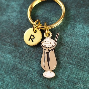 Puede incluir: Llavero dorado con un dije de batido de chocolate y un dije dorado con la letra R.