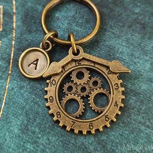 May include: A brass keychain with a round charm that says "A" and a larger charm with a gear design and the numbers 1 through 12.