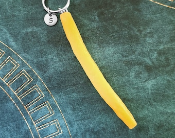 May include: A yellow, long, skinny, french fry keychain with a silver keychain ring and a silver charm with the letter "S" on it.