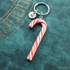 May include: A red and white candy cane keychain with a silver letter 'N' charm. The keychain is on a teal background.