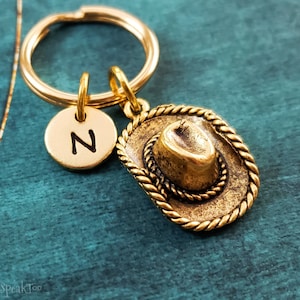 May include: Gold-toned keychain with a small letter 'N' charm and a cowboy hat charm.