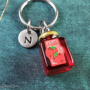 May include: A silver keyring with a letter N charm and a small glass jar charm with a red strawberry jam label. The jar charm has a gold lid.