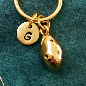 May include: Gold-toned keychain with a small, round charm engraved with the letter "G" and a charm shaped like a potato.