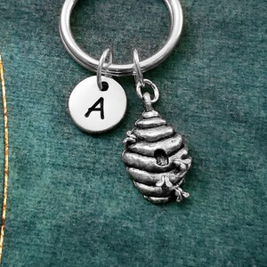 May include: Silver keychain with a beehive charm and a round charm with the letter A.