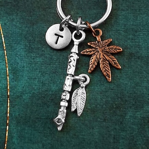 May include: Silver keychain with a charm of a peace pipe, a feather, a marijuana leaf, and a silver charm with the letter T.