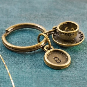 May include: A bronze key chain with a small teacup and saucer charm and a round charm with the letter "B" engraved on it.