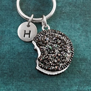 May include: A silver key chain with a black and white glitter cookie charm and a silver charm with the letter H.