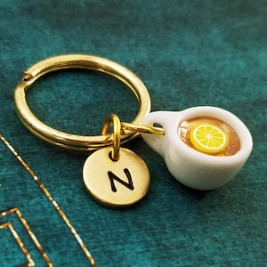 May include: Gold keychain with a small white teacup charm with a lemon slice and a gold disc charm with the letter N.