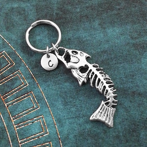 May include: Silver fish skeleton keychain with a silver charm that has the letter C on it.