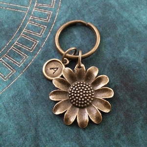 May include: A bronze key chain with a sunflower charm and a letter 'A' charm. The sunflower charm has a detailed center and petals.