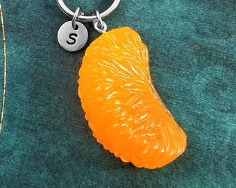 May include: A silver keychain with a letter 'S' charm and a bright orange, realistic-looking tangerine slice charm.
