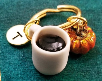 May include: A gold key chain with a small white mug filled with black coffee, a small orange pumpkin charm, and a gold charm with the letter "T" on it.