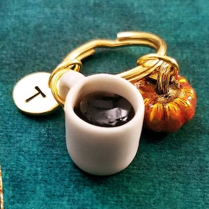 May include: A gold key chain with a small white mug filled with black coffee, a small orange pumpkin charm, and a gold charm with the letter "T" on it.