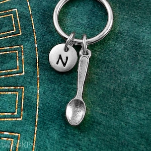 May include: A silver keychain with a small spoon charm and a round charm with the letter N on it.