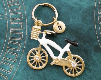 May include: Gold-tone bicycle keychain with a white bicycle, a black seat, and a small basket. The keychain has a gold-tone ring and a round charm with the letter "B" on it.
