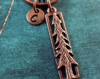 May include: Copper keychain with a letter C charm and a charm with a detailed cutout of a pine tree.
