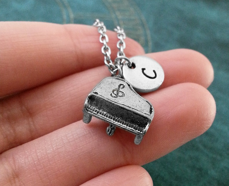 Op de afbeelding: Zilveren ketting met een kleine pianobedel en een ronde bedel met de letter C erop gegraveerd.